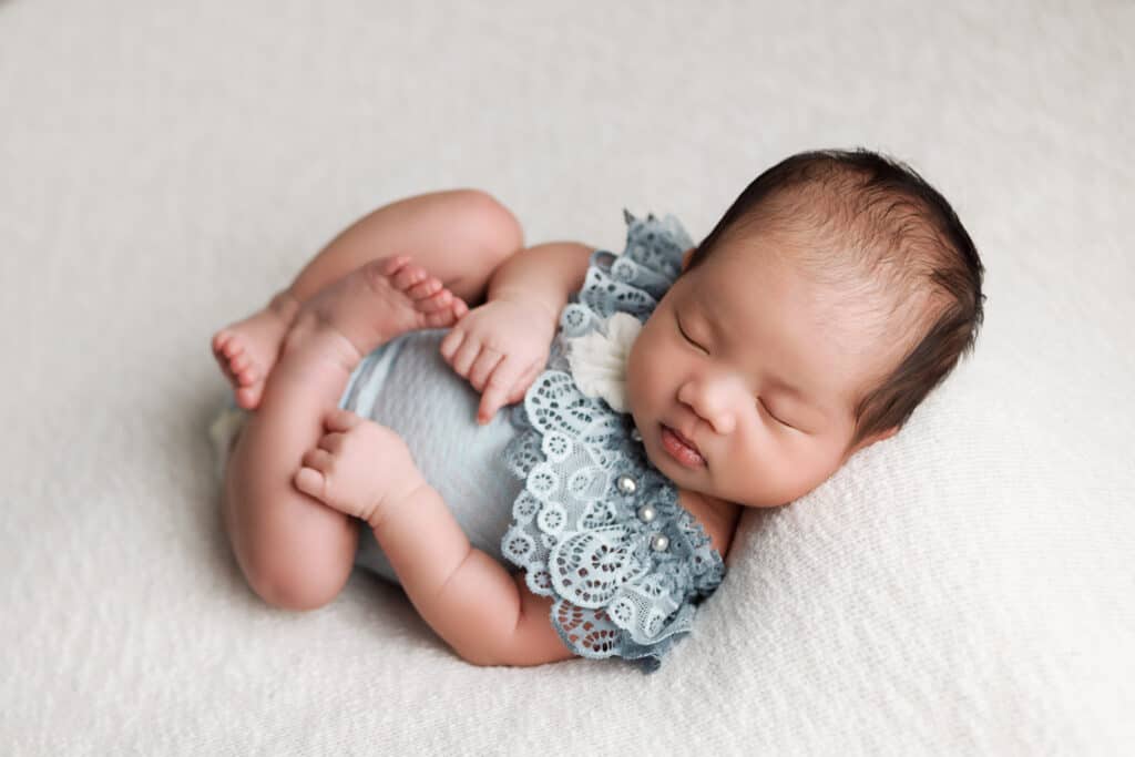 newborn portrait on ivory backdrop with blue lace romper