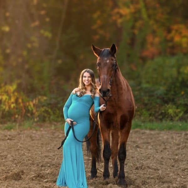 Windham NH Maternity in blue dress at horse farm leaning up against horse