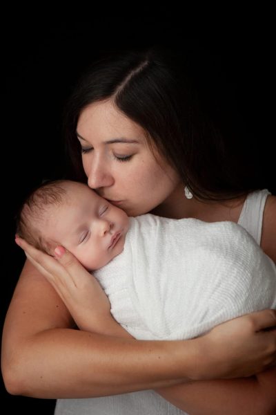 Baby AJ Mom kissing baby on black backdrop