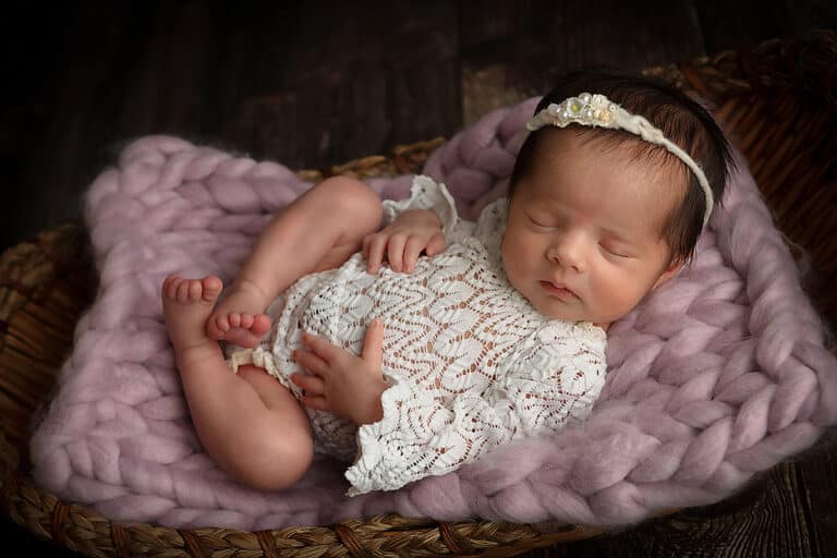 Preparing for your newborn portrait session in ivory lace romper in a basket