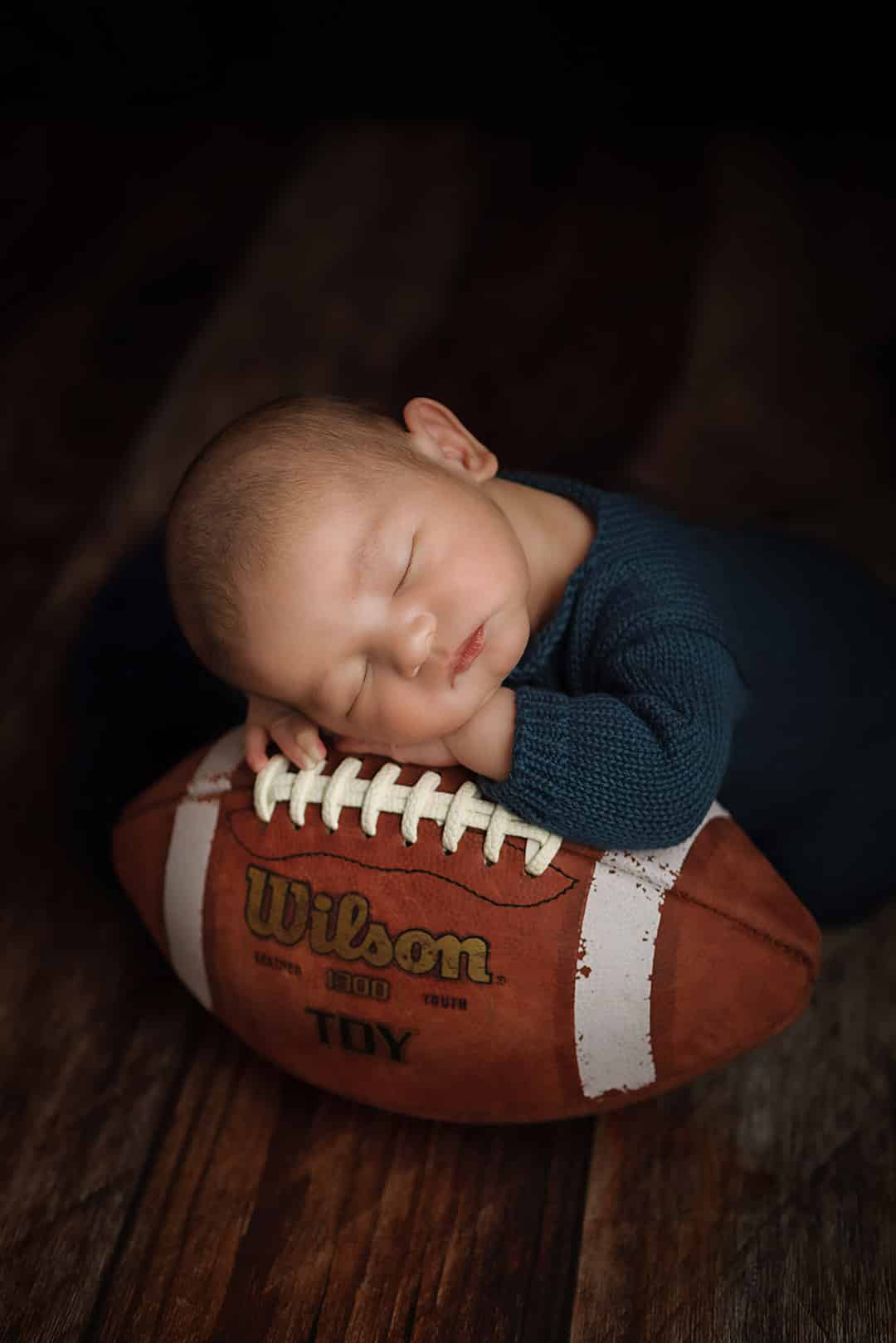 Windham NH Newborn Portrait. Baby sleeping with head on hands laying on a football.
