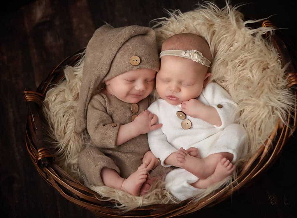 Windham NH Newborn twin portrait. Baby boy in a tan knit romper and baby girl in a white knit romper snuggled close together in a basket filled with fur sleeping.