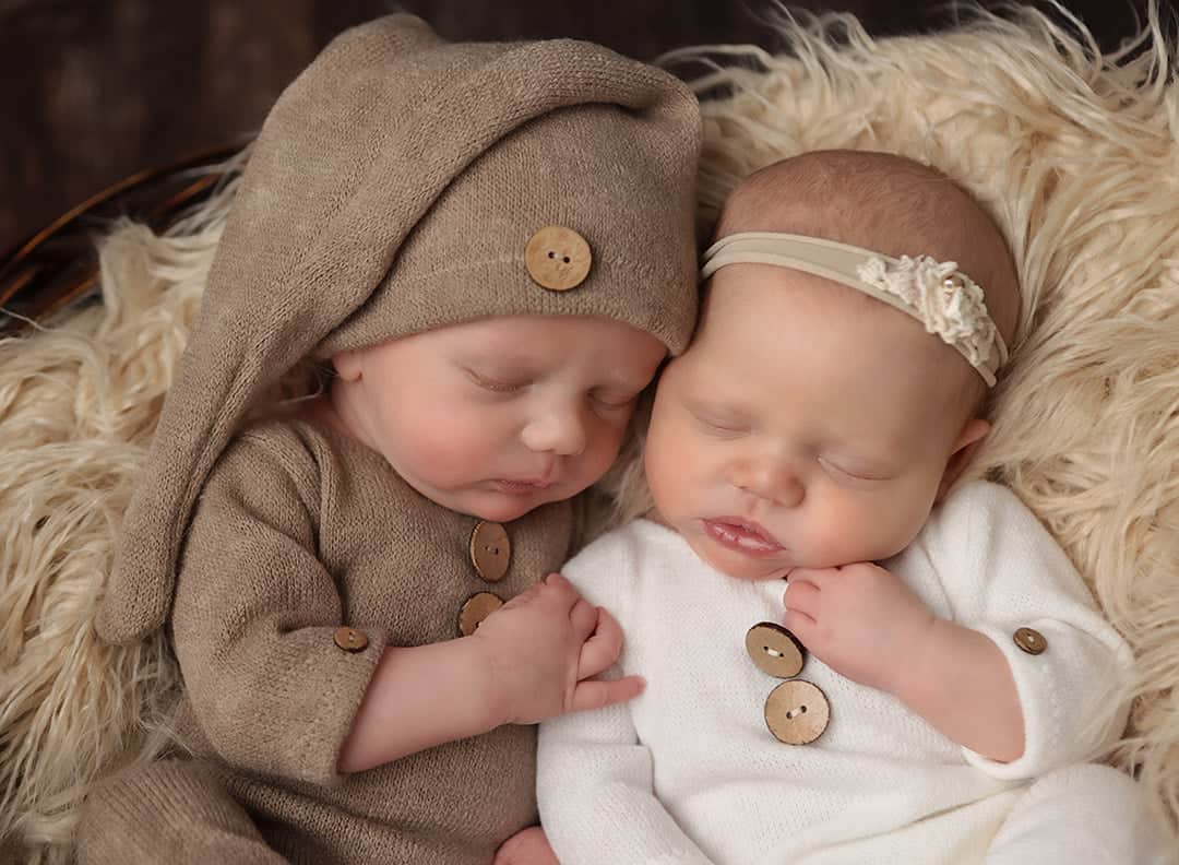 Windham NH Newborn twin portrait. Baby boy in a tan knit romper and baby girl in a white knit romper snuggled close together in a basket filled with fur sleeping.