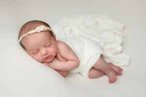 Newborn Baby Girl from Concord MA. Portrait of her laying on her side with an ivory wrap and pearl knit headband.