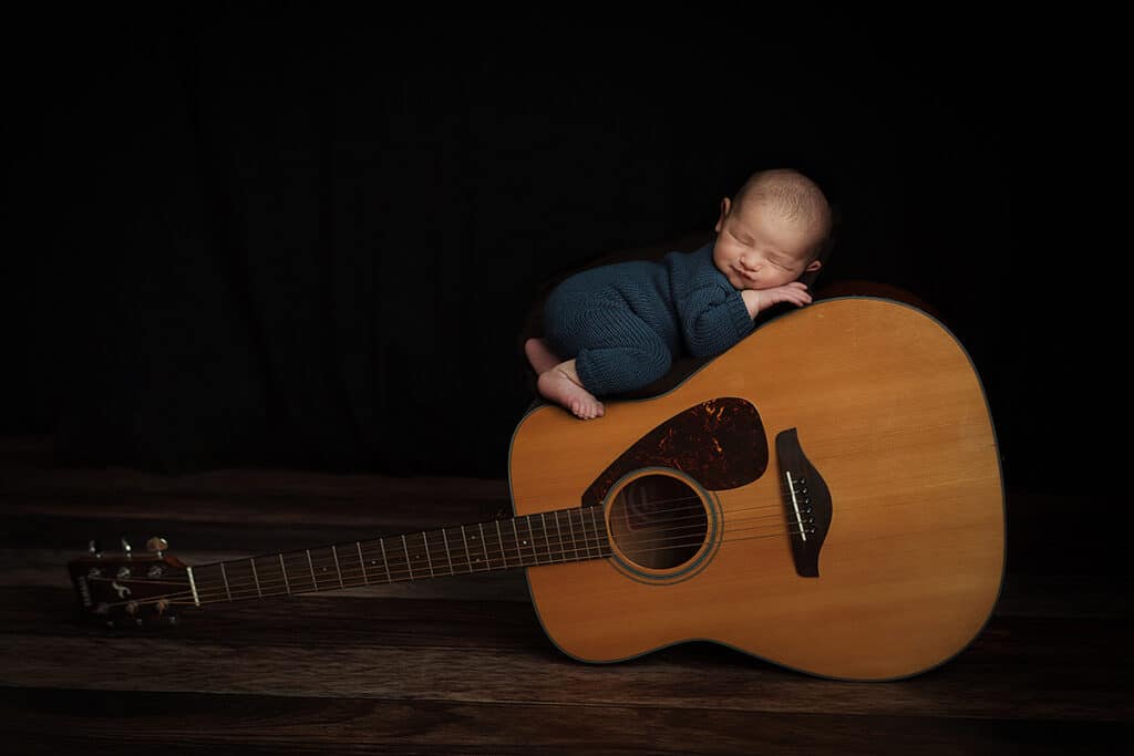 Derry NH Newborn Portrait of baby boy in a navy blue knit romper sleeping on a guitar. 