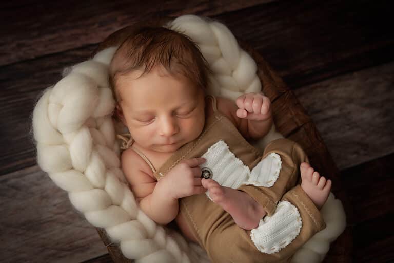Derry NH Newborn Portrait baby boy in tan romper with ivory pockets. Baby is laying in a wooden bowl with ivory knit blanket. He is sleeping.