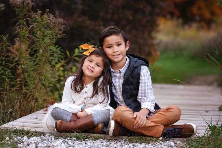 Fall Family Mini Session of Brother and Sister sitting on wooden bridge smiling.
