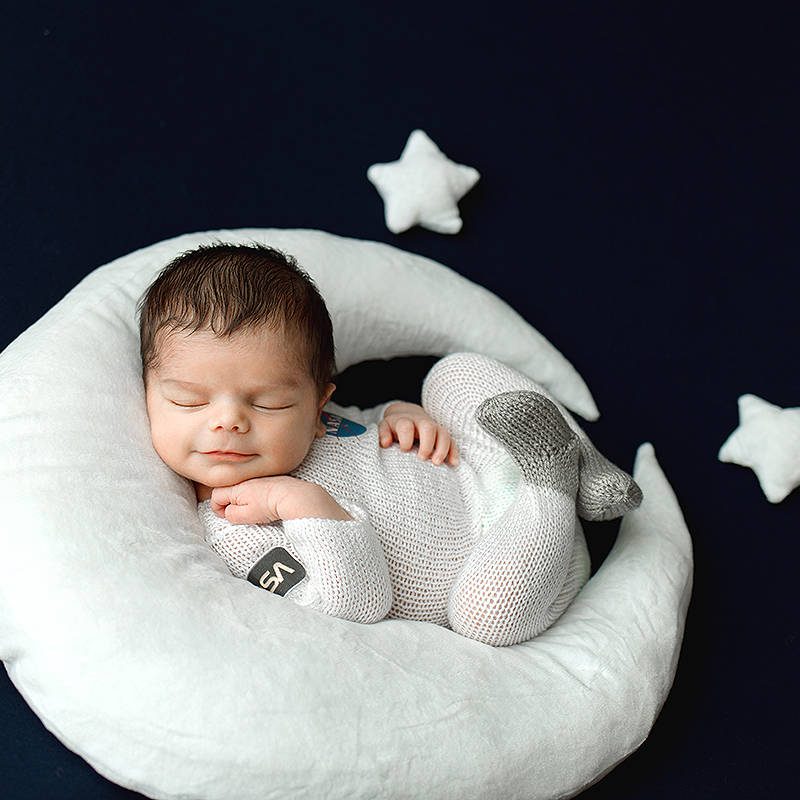 Newborn Baby Boy sleeping on a plush moon prop wearing a hand knit astronaut outfit.