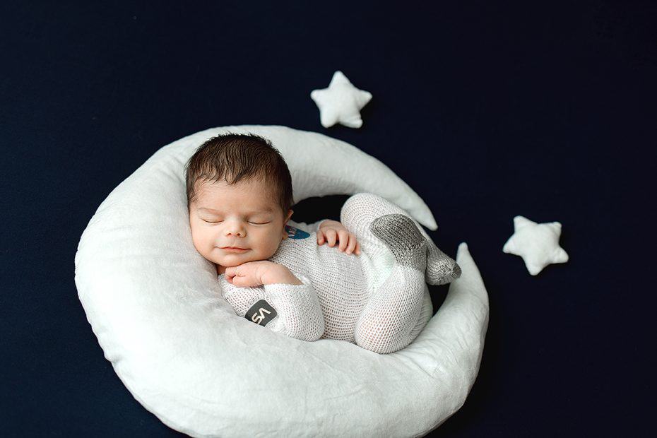 Newborn Baby Boy sleeping on a plush moon prop wearing a hand knit astronaut outfit.