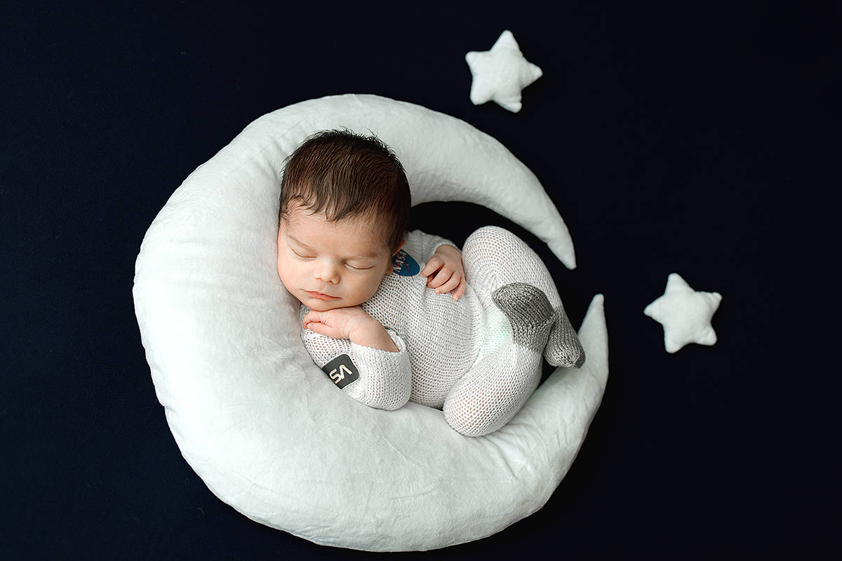 Newborn Boy sleeping on a plush moon prop with stars, wearing a hand knit astronaut outfit.