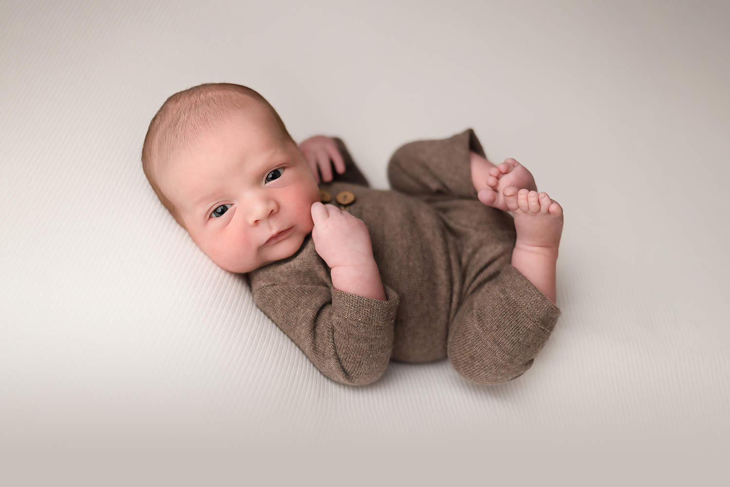 NH Newborn Portrait - Baby Boy in knit brown romper looking at the camera.