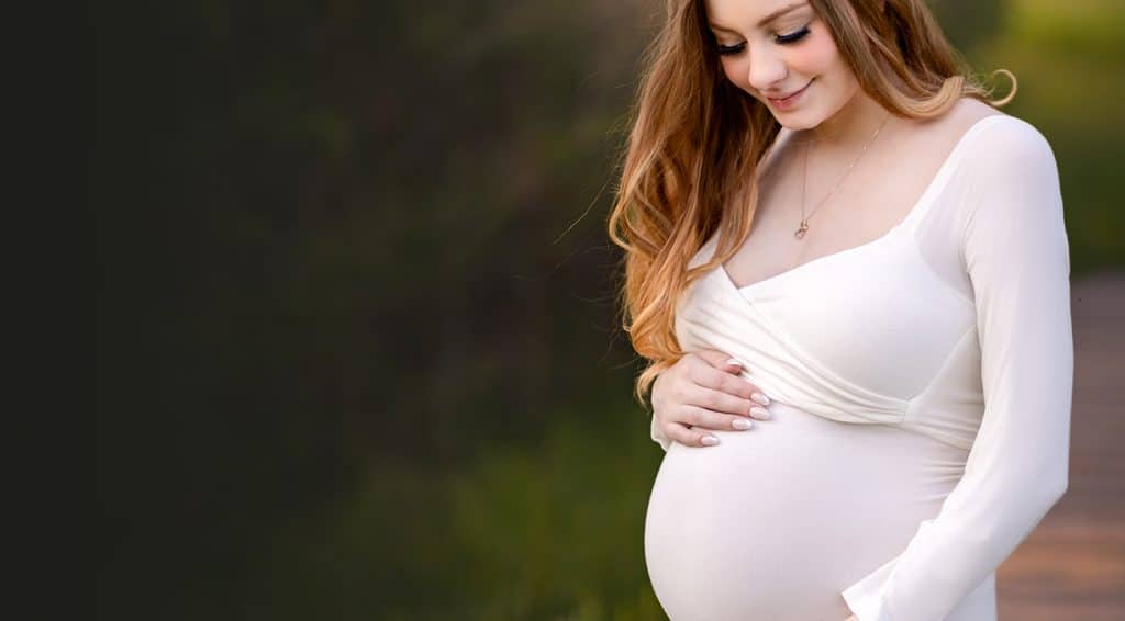 Boston Maternity Session - mother in white couture maternity gown posing for an outdoor maternity session looking down at her baby bump.