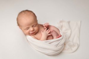 Salem NH newborn portrait of baby girl laying on ivory background with an ivory wrap laying in a womb like pose.