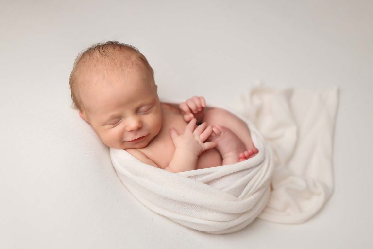 Salem NH newborn portrait of baby girl laying on ivory background with an ivory wrap laying in a womb like pose.