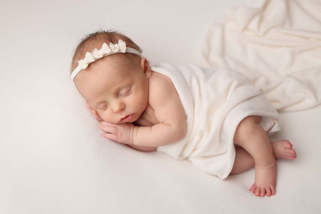 Salem NH Newborn portrait of baby girl laying on her side with ivory wrap and ivory background.