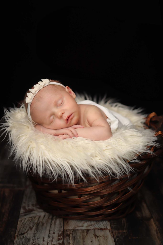 Salem NH newborn portrait of baby girl laying in a basket filled with ivory faux fur with her arms crossed under her chin.