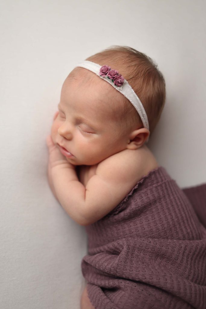 Salem NH Newborn portrait of baby girl laying on her side with a purple wrap over her side.