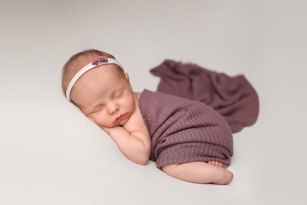 Salem NH Newborn Portrait of baby girl wrapped in a purple wrap laying on her tummy.