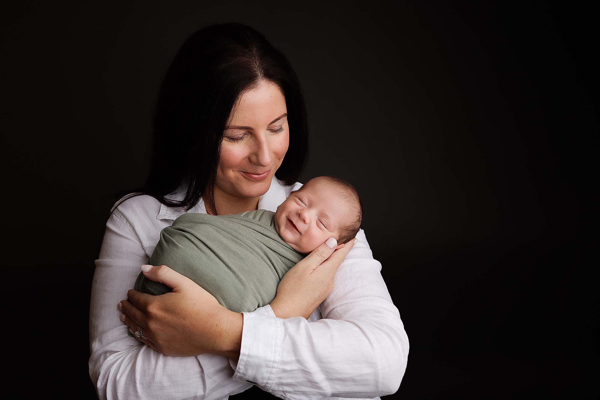 newborn in a sage green wrap held by mother.