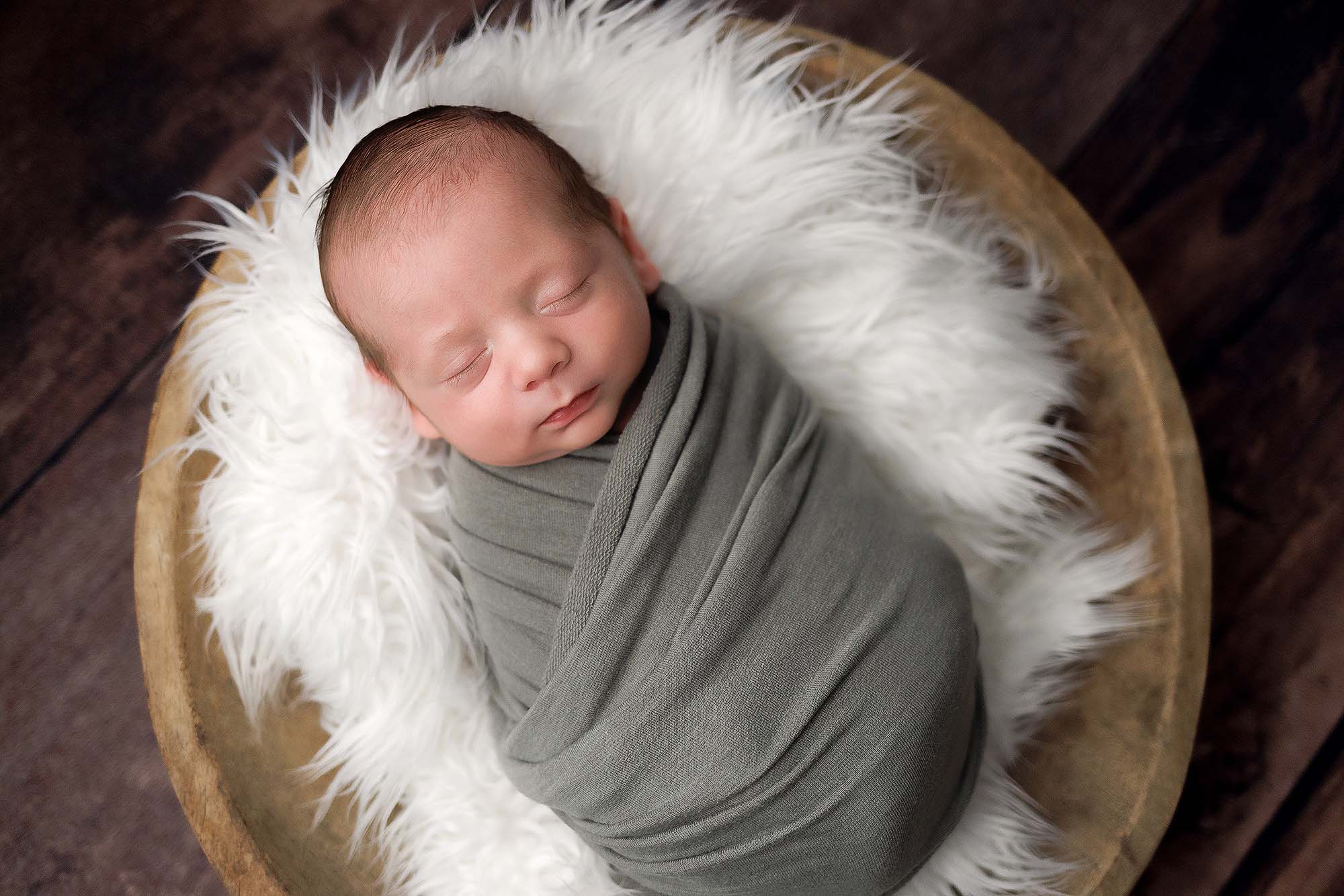 Andover, MA newborn portrait of baby boy wrapped in a sage green wrap sleeping in a wooden bowl.