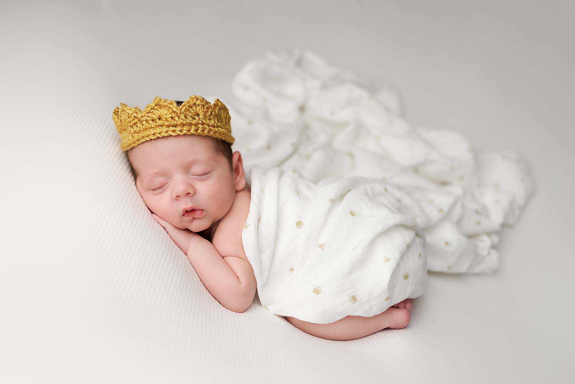 Newborn Portrait of baby boy in an ivory wrap wearing a knit gold crown.