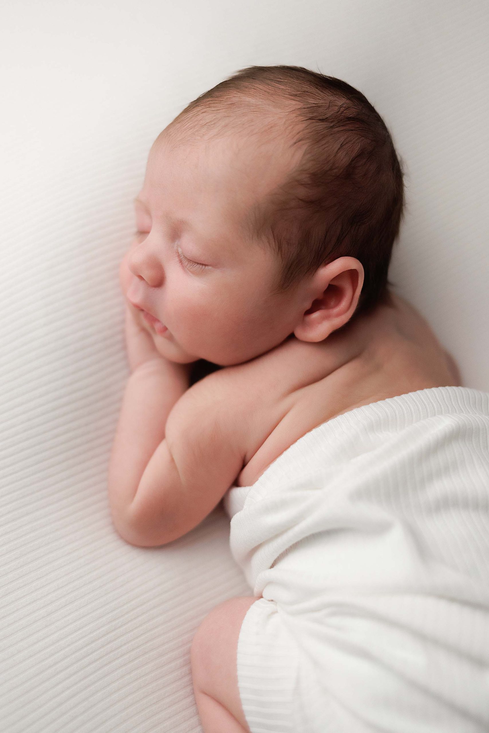 Baby boy posing for a newborn portrait wrapped in an ivory wrap on an ivory background.