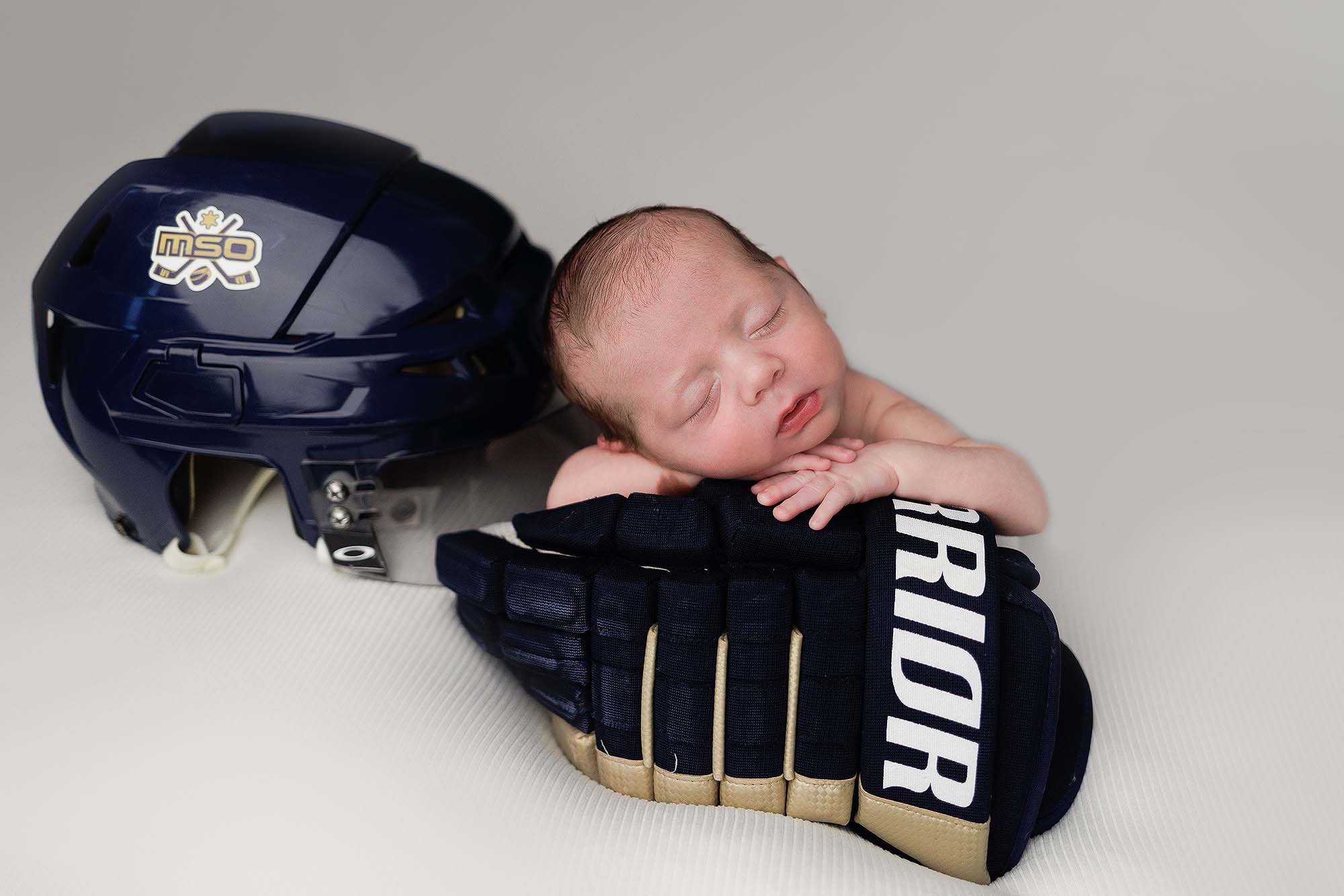 Newborn portrait of baby boy propped up and posed with a large hockey glove.