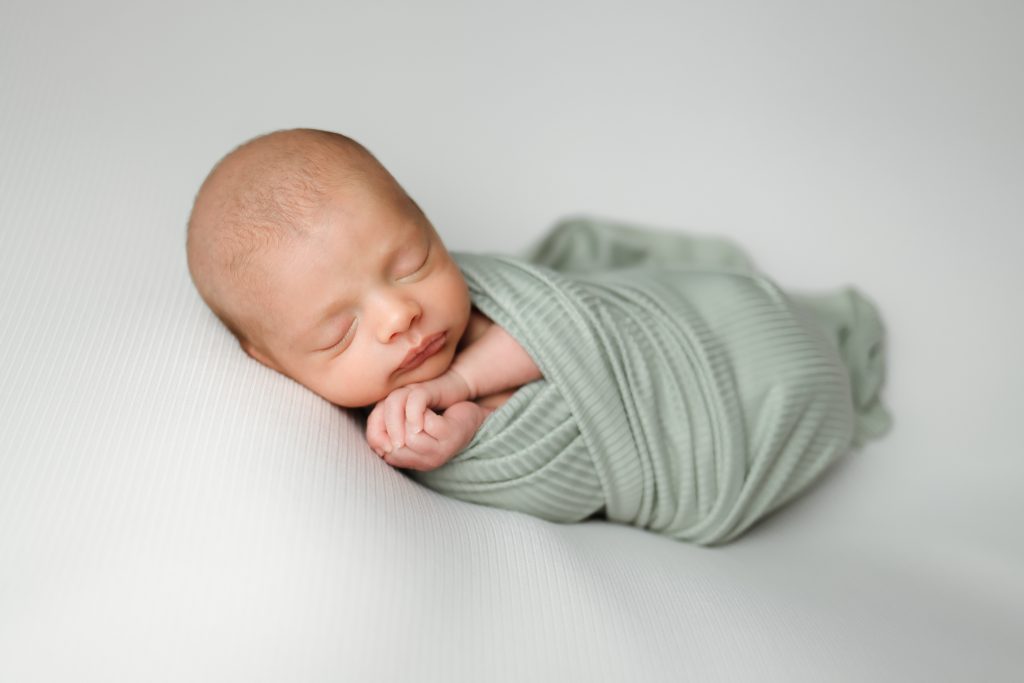 Boston Newborn portrait of baby boy swaddled in a sage green wrap laying on side.