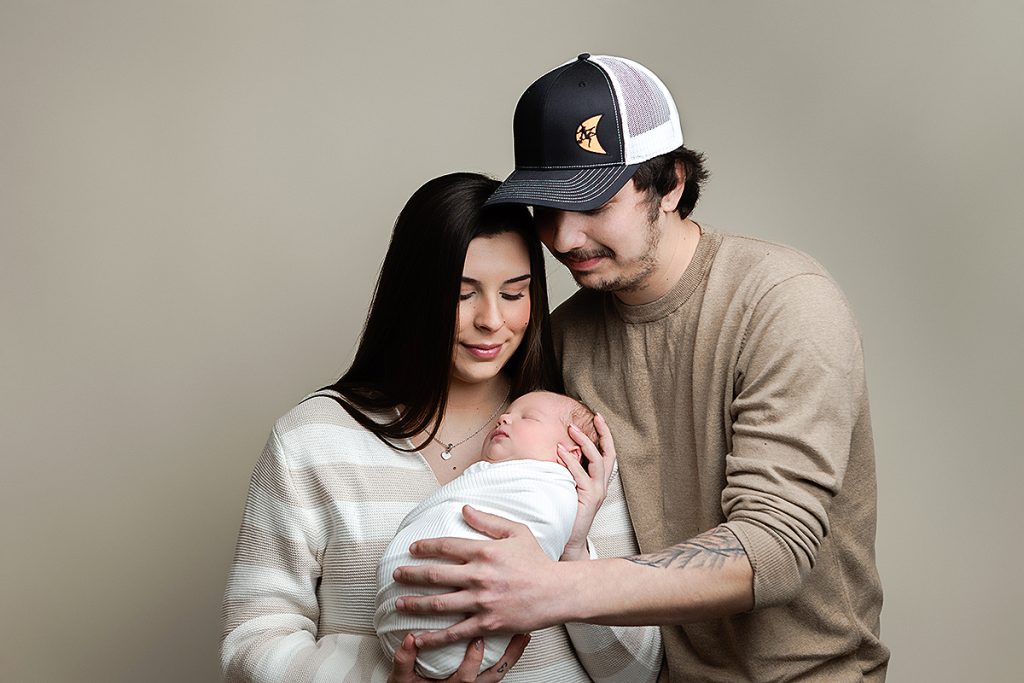 Boston Metro Area Newborn Portrait of mother and father holding newborn wrapped in ivory wrap.