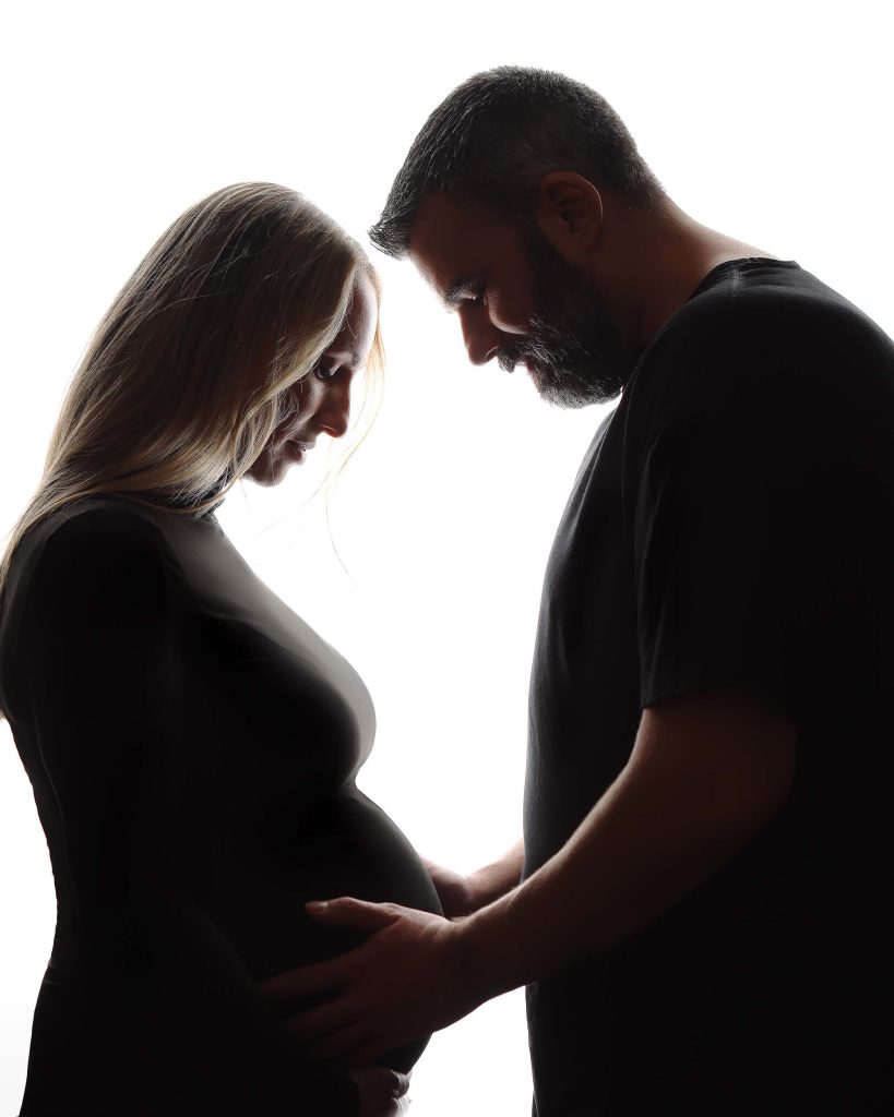 Boston Maternity Portrait of mother-to-be posing with husband. Backlit image.