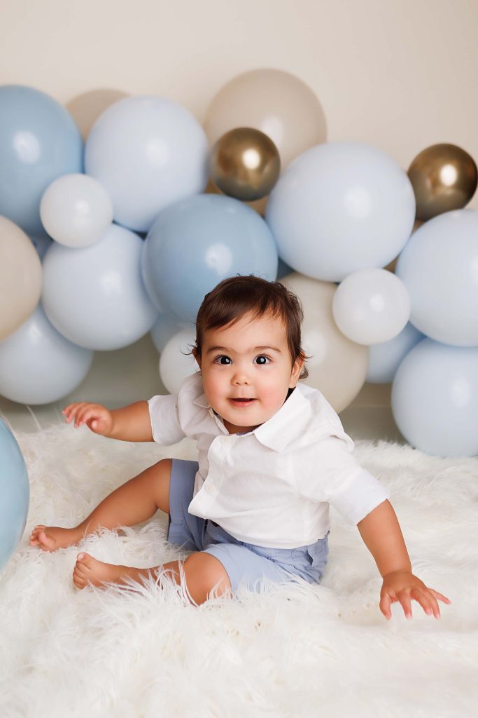 One Year old sitting on white fur throw for a cake smash session.