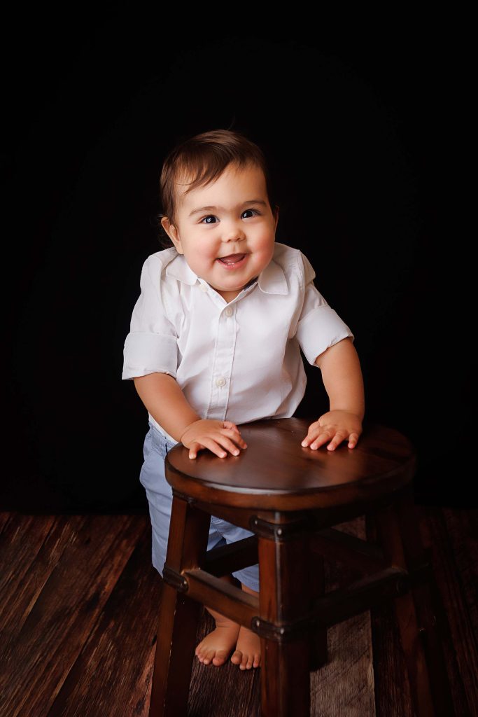 One year old standing and holding a wooden stool for a one year portrait.