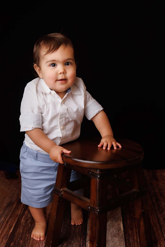 One year old standing and holding a wooden stool for a one year portrait.