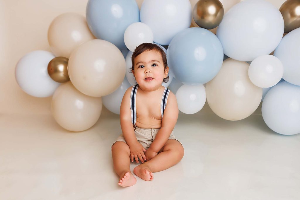 One year old smiling at camera in front of balloon garland.