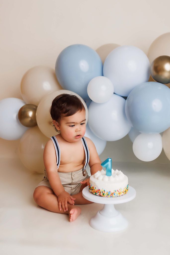 One year old looking at birthday cake for a cake smash portrait.