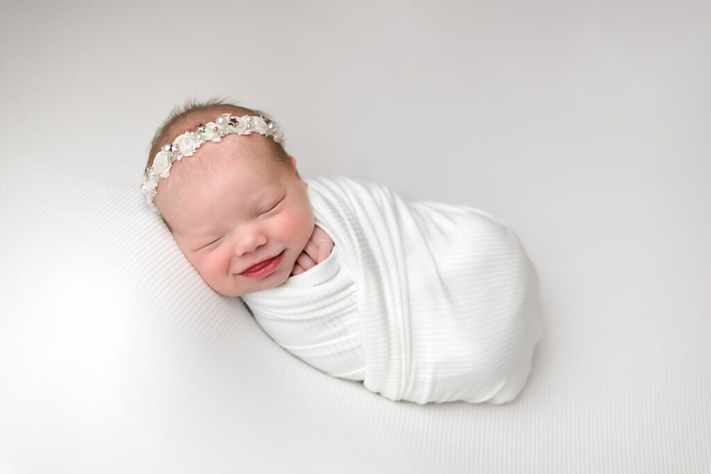 NH Newborn Photographer - Newborn girl wrapped in ivory wrap, smiling.
