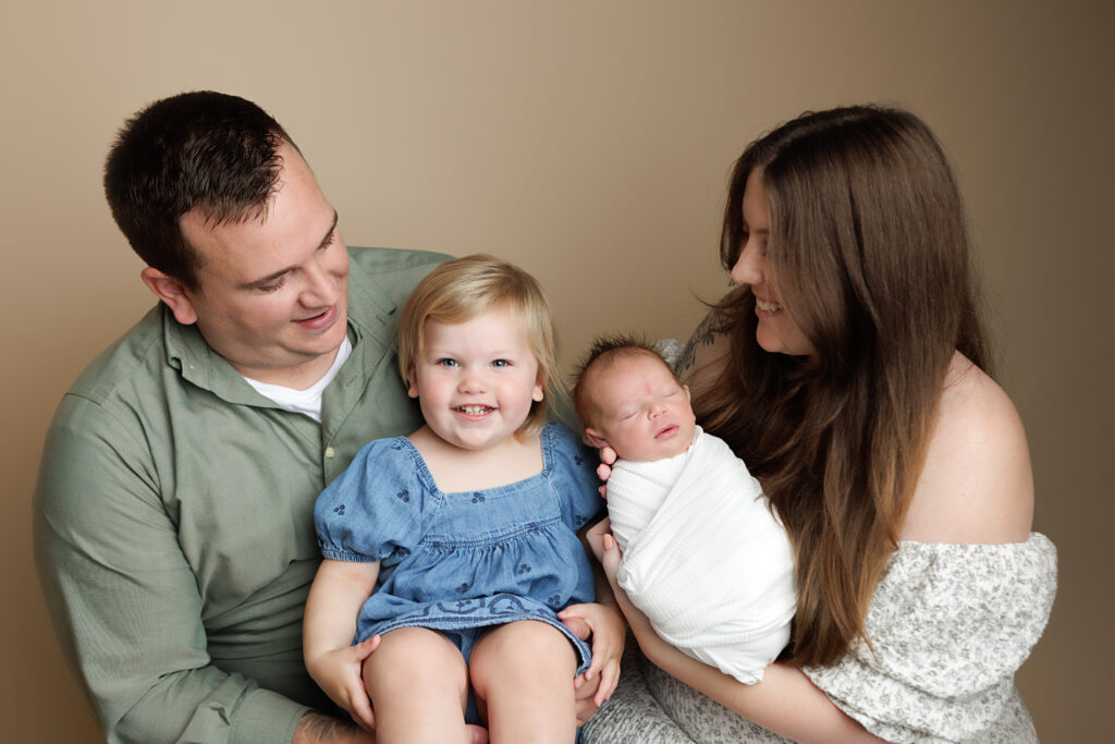 Family Portrait during a newborn session. Boston Newborn Portrait of toddler smiling at camera while mom and dad are holding newborn sister.