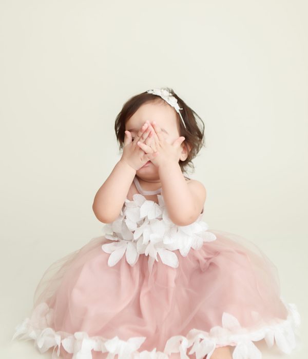 Boston Cake Smash portrait session of little girl covering her face with her hands hiding from the camera.