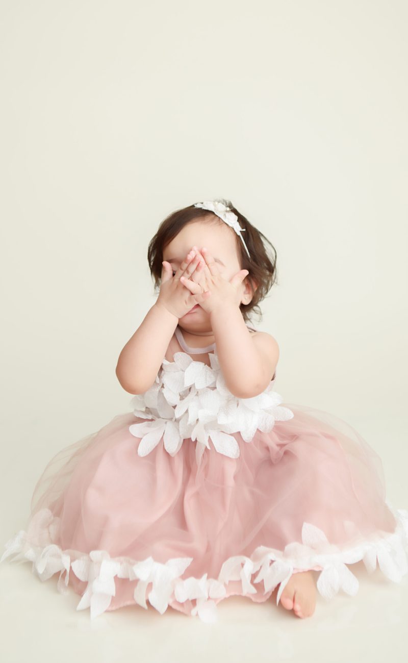Boston Cake Smash portrait session of little girl covering her face with her hands hiding from the camera.