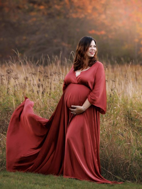 Maternity Portrait of expectant mother wearing orange maternity dress in field with NH fall foliage