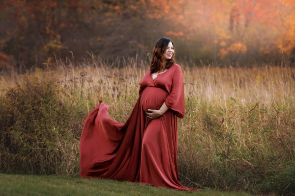 Maternity Portrait of expectant mother wearing orange maternity dress in field with NH fall foliage