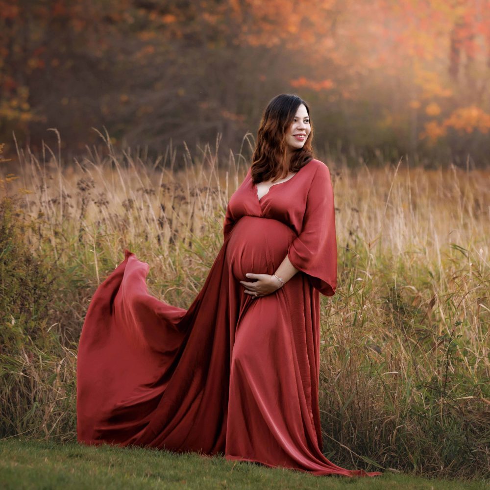 Maternity Portrait of expectant mother wearing orange maternity dress in field with NH fall foliage