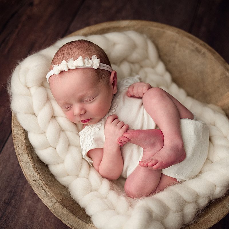 Boston Newborn Portrait of baby girl in an ivory outfit laying in a wooden bowl.