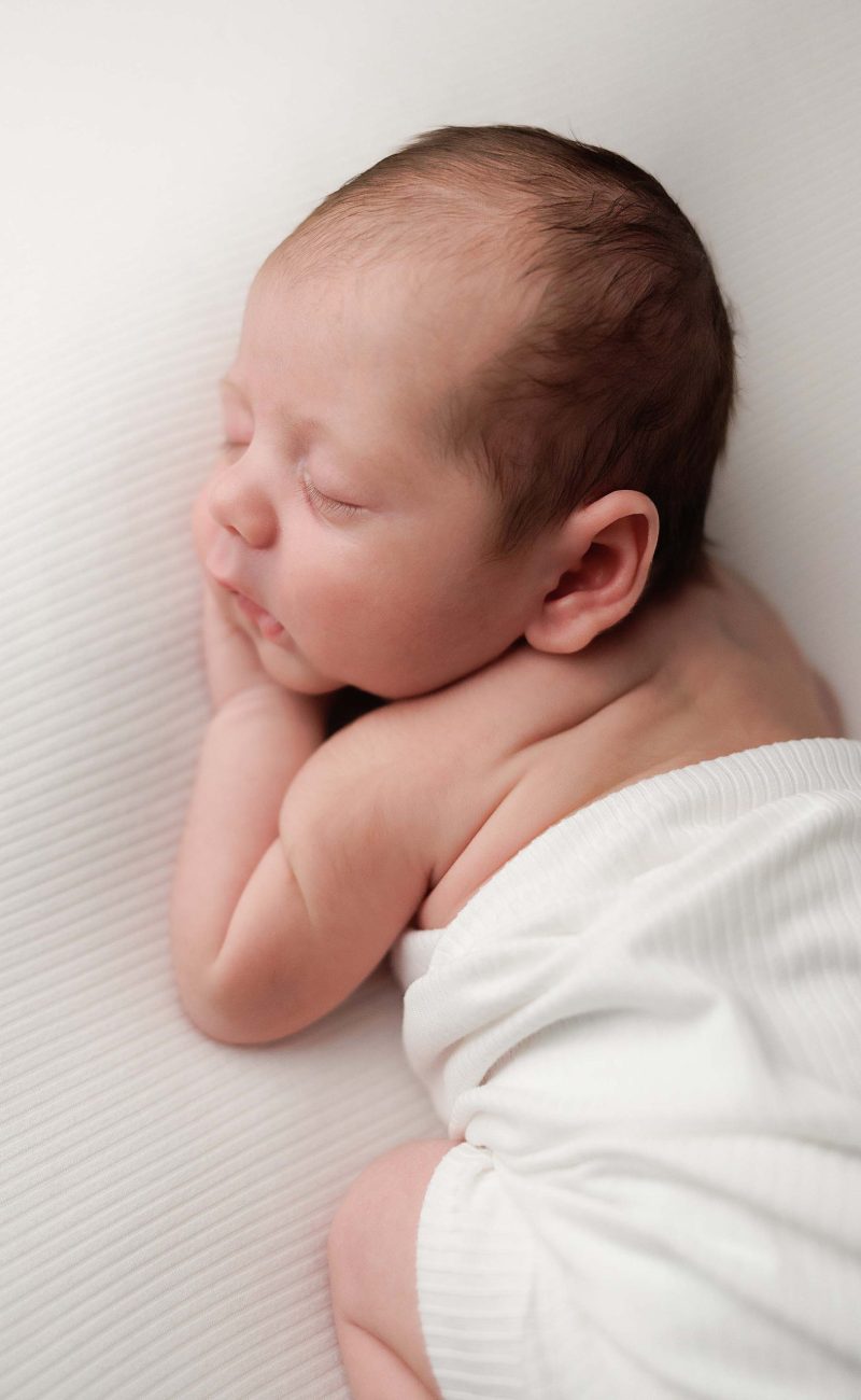Baby boy posing for a newborn portrait wrapped in an ivory wrap on an ivory background.