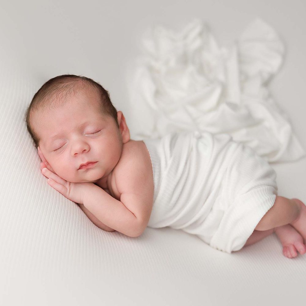 Newborn wrapped in a ivory wrap in a side pose with hands tucked under cheeks.