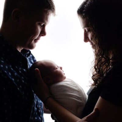 Backlit Image of mother and father looking at newborn. Boston Newborn Portrait Session