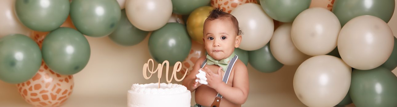 One Year little boy eating cake for his NH cake smash session with green and animal print balloon garland.
