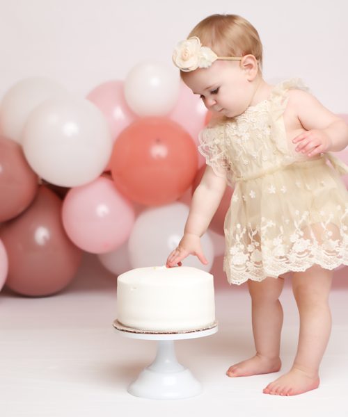 One year old girl eating standing next to her birthday cake for a cake smash in NH.