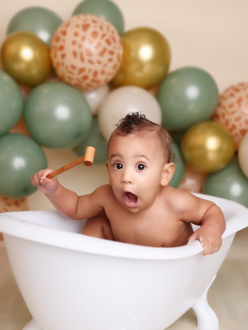 Boston cake smash portrait of little boy in mini tub filled with bibbles. sage green and safari printed balloon garland in background.