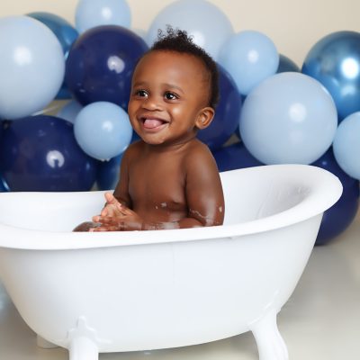 Boston Cake smash portrait of little boy taking a buble bath. Blue balloon garland in background.